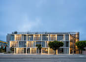 Thumbnail 4 of 9 - A modern building with a glass facade and a tree in front of it.