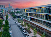 Thumbnail 12 of 16 - A parking lot with cars and a building with large windows.