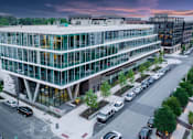 Thumbnail 10 of 16 - A modern glass building with cars parked in front.