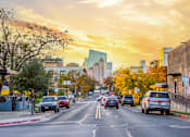 Thumbnail 15 of 16 - A city street with cars and buildings under a cloudy sky.