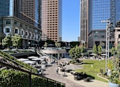 Thumbnail 8 of 18 - A city park with people walking around and tall buildings in the background.