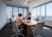 Thumbnail 17 of 18 - A woman is giving a presentation to two people at a conference table in a room with a city view.