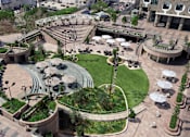 Thumbnail 2 of 18 - A large, circular, outdoor seating area is surrounded by a grassy hill and a building.