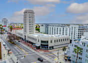 Thumbnail 12 of 17 - A tall white building with a pointed top is in the middle of a city intersection.