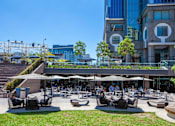 Thumbnail 21 of 27 - A large outdoor seating area with people dining and a modern building in the background.