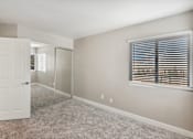 Thumbnail 11 of 23 - A room with a white door, carpeted floor, and a window with blinds.