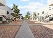 Thumbnail 16 of 23 - A long concrete walkway separates two rows of white buildings with trees in between.
