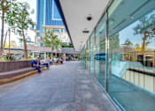 Thumbnail 18 of 27 - A glass-walled building with people sitting on benches outside.
