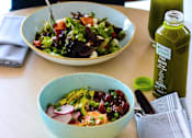Thumbnail 6 of 18 - A person is eating a salad with a lemon wedge and a bottle of green juice on the table.