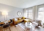 Thumbnail 1 of 30 - A living room with a brown couch, a coffee table, and a round mirror on the wall.