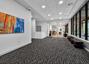 Thumbnail 9 of 38 - A large abstract painting hangs on a white wall in a spacious room with grey carpeting.