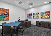 Thumbnail 4 of 38 - A conference room with a blue table and chairs, a desk with a chair, and three paintings on the wall.