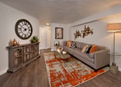 Thumbnail 16 of 51 - A living room with a grey couch, a wooden cabinet, a clock, and a rug.