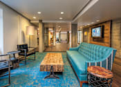 Thumbnail 7 of 51 - A blue couch sits in a room with a wooden table and a TV mounted on the wall.