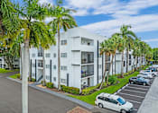 Thumbnail 21 of 52 - A white apartment building with a parking lot in front of it.