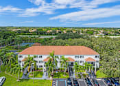 Thumbnail 27 of 52 - A large white building with a red roof is surrounded by greenery and has a parking lot in front.