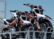 Thumbnail 13 of 13 - A trailer loaded with four motorcycles is parked.