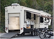 Thumbnail 12 of 13 - A white RV is parked next to a black motorcycle.