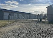 Thumbnail 8 of 13 - A gravel area in front of a grey building with a fence and gate.
