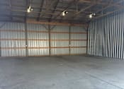 Thumbnail 10 of 10 - A large, empty warehouse with a concrete floor and a corrugated metal wall.
