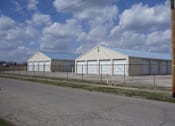 Thumbnail 1 of 10 - A large white building with a grey roof and a fence in front of it.