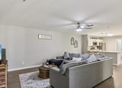Thumbnail 31 of 33 - A living room with a grey couch and a ceiling fan.