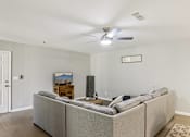 Thumbnail 30 of 33 - A living room with a grey couch and a ceiling fan.