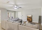 Thumbnail 29 of 33 - A living room with a grey couch and a ceiling fan.