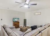 Thumbnail 28 of 33 - A living room with a grey couch and a ceiling fan.
