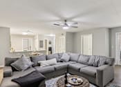 Thumbnail 27 of 33 - A grey sectional sofa with a black throw pillow sits in a living room with a ceiling fan and a coffee table.