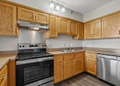 Thumbnail 13 of 22 - Irvine Park Towers apartment kitchen with wood cabinetry, light countertops and white appliances