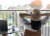 Thumbnail 6 of 8 - A woman in a hat is sitting on a chair with her back to the camera, looking out of a balcony.at Sylk Towers, Kitchener, ON N2A 1B1