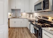Thumbnail 1 of 26 - A modern kitchen with white cabinets and a black stove top.