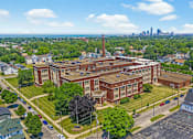 Thumbnail 29 of 29 - A large red brick building with a tall chimney is surrounded by green trees and grassy areas.