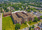 Thumbnail 28 of 29 - An aerial view of a large red brick building with a green lawn in front.