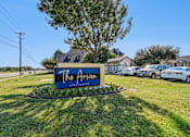 Thumbnail 16 of 17 - A sign for "The Arrow Apartments" is displayed in front of a grassy area with a tree and parked cars.