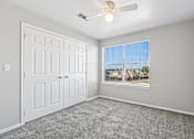 Thumbnail 7 of 17 - A room with a white door, a ceiling fan, and a window showing a view of houses.