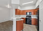 Thumbnail 9 of 17 - A kitchen with brown cabinets and black appliances.