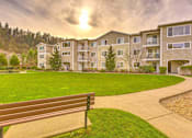 Thumbnail 2 of 19 - A bench is in the foreground of a grassy area in front of apartment buildings at Valley Springs Apartments, Renton, WA, 98058