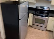 Thumbnail 8 of 16 - A black refrigerator stands next to a silver oven in a kitchen.