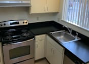 Thumbnail 7 of 16 - A kitchen with a stove, sink, and cabinets.