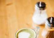 Thumbnail 14 of 42 - A cup of green tea latte with milk on a saucer.