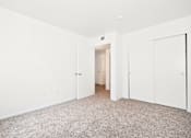 Thumbnail 18 of 30 - A white room with a carpeted floor and a door on the left.
