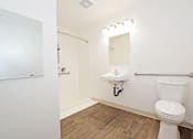 Thumbnail 16 of 42 - A white toilet in a small bathroom with wood flooring and a white sink.