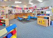 Thumbnail 11 of 17 - A classroom with tables and chairs and a blue carpet.