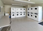 Thumbnail 22 of 35 - A laundry room with a row of washers and dryers.