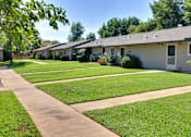 Thumbnail 2 of 35 - A row of houses with green lawns and trees in the background.