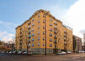 Thumbnail 1 of 29 - A yellow building with a green base and a parking lot in front.