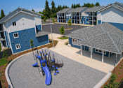 Thumbnail 2 of 10 - A playground area with a blue slide is surrounded by apartment buildings.