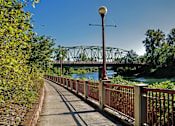 Thumbnail 7 of 11 - A bridge over a river with a metal railing and a lamp post on the sidewalk.